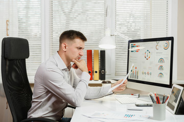 Serious and engrossed business man in shirt sitting at the desk, working at computer with modern...