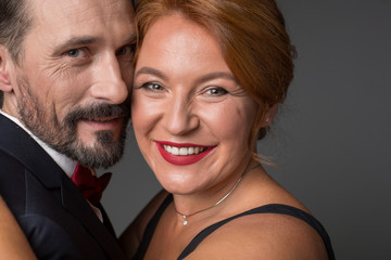 Portrait of happy middle-aged man and woman cuddling and smiling. They are standing in formalwear. Isolated