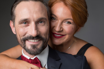 Portrait of happy married couple standing and hugging. They are looking at camera with joy and smiling. Lovers are wearing formal clothing