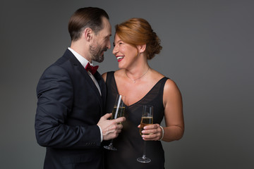 Waist up portrait of excited adult loving couple celebrating special occasion with champagne. They are looking at each other and laughing. Isolated