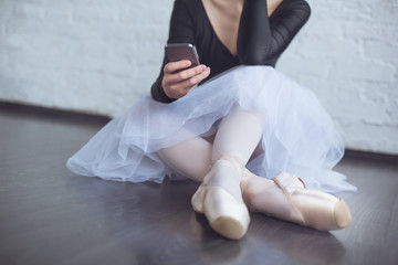 Young ballet dancer sitting leaning white wall using phone in studio active lifestyle close-up