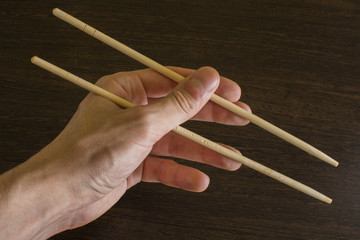 The left hand of a man using bamboo chopsticks on a wooden background