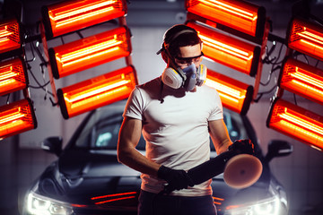 man wearing protective mask and glasses holding polishing machine with red warm lights in background