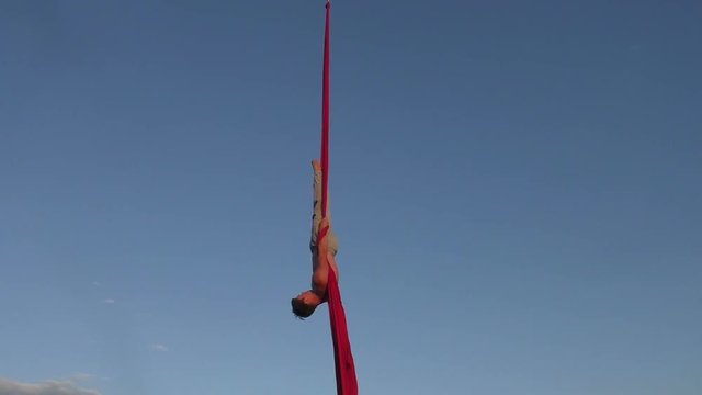 Male aerial acrobat shows tricks on canvases in the sky.
