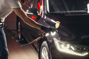 man wear protective mask and eyewear at work. Automobile industry. Car wash and coating business with ceramic coating polishing. Spraying varnish to car.