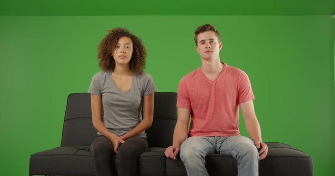 Boring couple staring at the camera on a futon couch on green screen. On green screen to be keyed or composited.