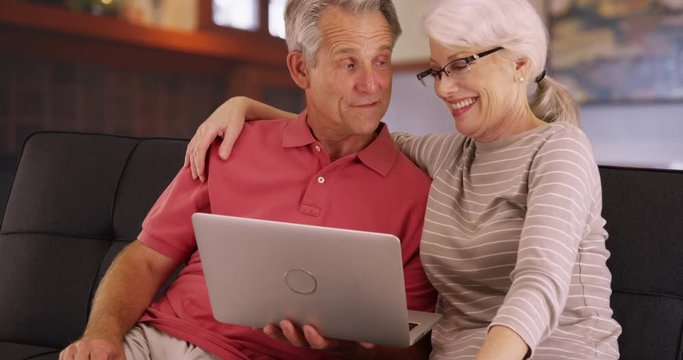 Cute elderly couple using laptop together at home