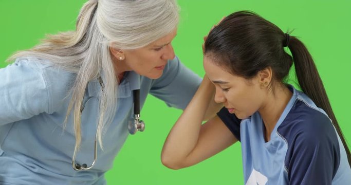 A medical professional attends to an injured soccer player on green screen. On green screen to be keyed or composited. 