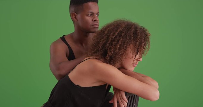 Black man and woman sitting together on green screen. On green screen to be keyed or composited. 