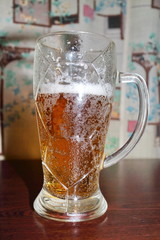 White beer foam in a glass on a dark table in front of a window