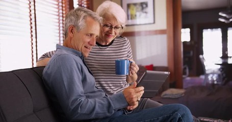 Modern senior couple sitting on couch with tablet - Powered by Adobe
