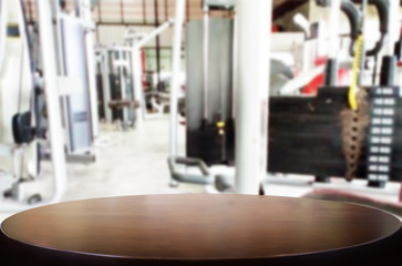 Fototapeta premium Wooden table on blurred background of fitness gym interior of modern club with equipment for your photomontage or product display.