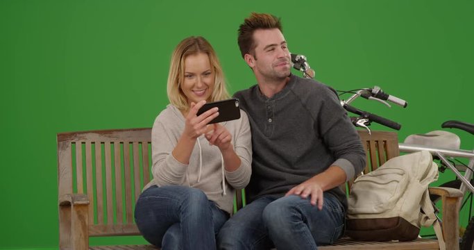 Happy Millennial couple watching videos on smartphone together on green screen. On green screen to be keyed or composited. 
