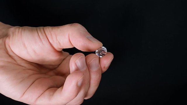 A man holds a diamond from small to huge in his hand and looks at it in the rays of light on black background. Closeup
