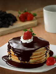Stack of pancakes with chocolate syrup, whipped cream and strawberries.