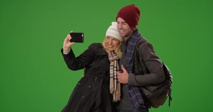 Happy yuccie couple taking a selfie in winter clothes on green screen. On green screen to be keyed or composited. 