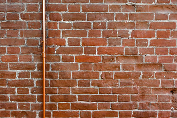 Obraz premium Old brick wall, texture of red stone blocks with pipe. Close up. Weathered red grungy brick wall background. Architecture detail. Copy space.