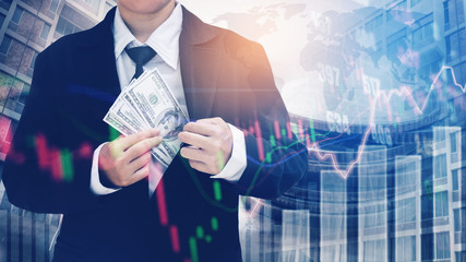 Businessman Holding money US dollar bills on digital stock market financial exchange and Trading graph Double exposure city on the background