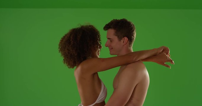 Interracial couple embracing in their swimsuits in contrasty lighting on green screen. On green screen to be keyed or composited. 