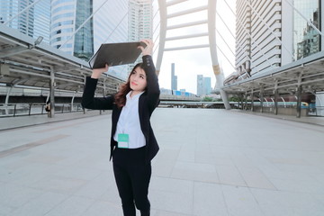 Obraz premium Attractive young Asian business woman walking and raising ring binder at sidewalk of urban city background.