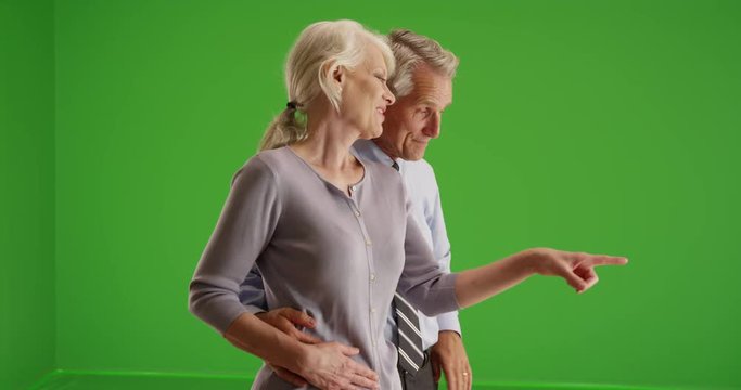 Elderly couple standing by window talking on green screen. On green screen to be keyed or composited. 