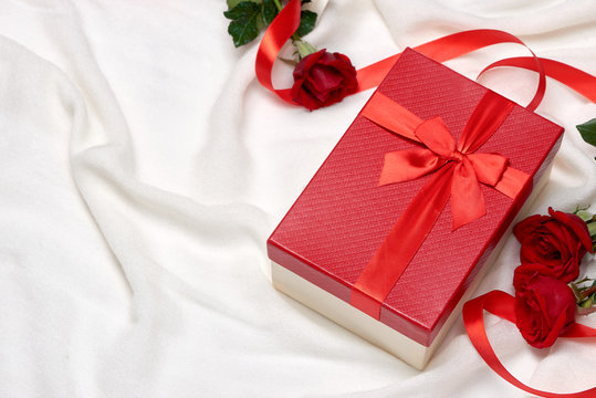 Red gift box with ribbon bow present and red roses on holiday