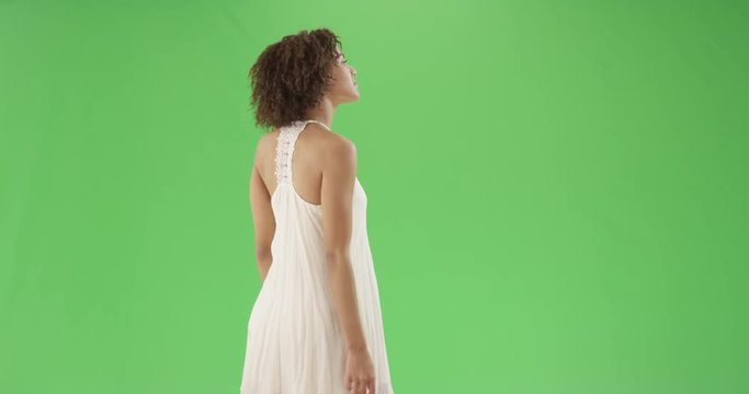 African American millennial girl looks up to the right in a sun dress on green screen. On green screen to be keyed or composited. 