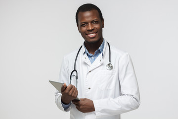 Indoor closeup of handsome African American doctor isolated on white background dressed in uniform with tablet PC in hands looking at camera with confident positive smile ready to work and help