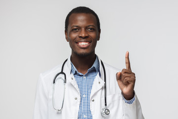 Horizontal closeup of young African American doctor pictured isolated on white background wearing uniform and holding index finger up as if having interesting idea or solution concerning treatment