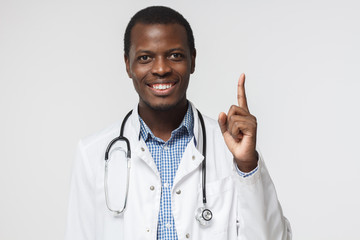 Attractive young african american doctor pointing up with his finger isolated on gray background