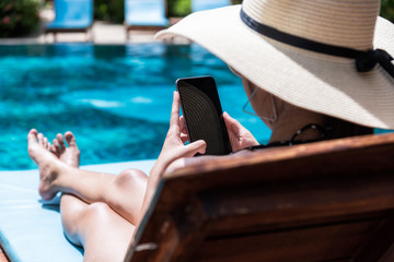 Young Beautiful lady wearing bikini using mobile phone sitting on chair in swimming pool