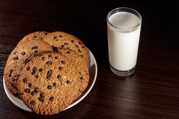 Chocolate chip cookies and glass of milk on wooden table