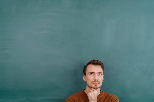 Young pensive man standing against blackboard