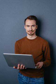 Young man standing with laptop on dark background
