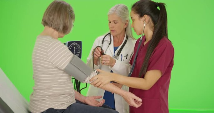 Female doctor teaching student nurse to take blood pressure with cuff on green screen. On green screen to be keyed or composited. 
