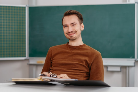 Young smiling man sitting at desk with binder