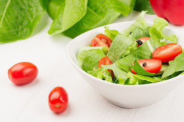 Fresh spring greens salad with cherry tomatoes and pepper on soft white wood plank, copy space, closeup.