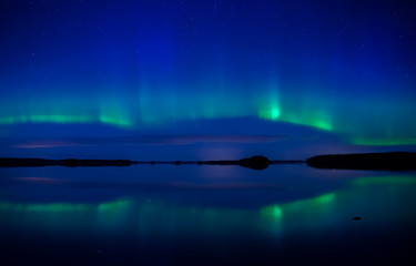 Northern lights dancing over calm lake in Farnebofjarden national park in Sweden.