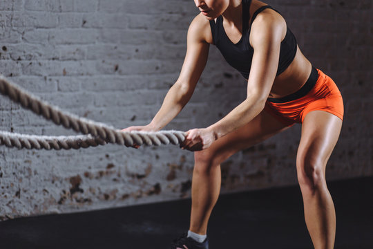 close up photo of woman doing Battle rope workout near white brick wall