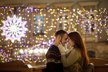 Young couple stands embracing against the shining festive garlands.