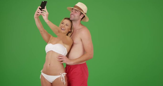 Happy millennial couple taking selfies by the beach on green screen. On green screen to be keyed or composited. 