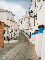 White narrow streets with whitewashed traditional andalusian houses, blue pots with red geranium at the walls at little touristic town village Mijas, Malaga province, Andalusia, Spain.