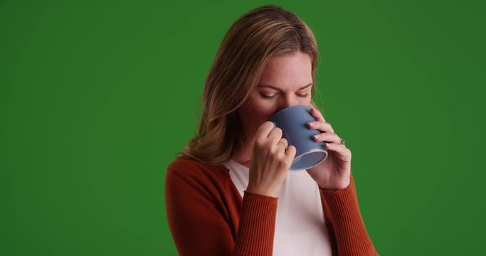 Caucasian woman drinking coffee or tea smiling at camera on green screen. On green screen to be keyed or composited.
