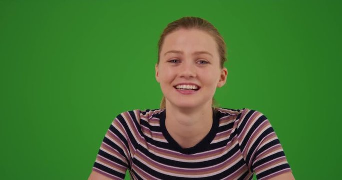 Young blonde millennial girl looking at camera and having video chat on green screen. On green screen to be keyed or composited. 