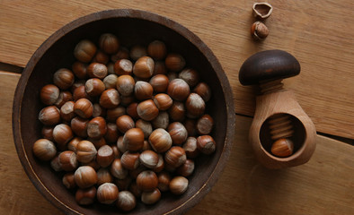 Wooden mushroom shape nutcracker and plate with hazelnuts, top view. Screw type nut cracker and hazelnuts on wood table.