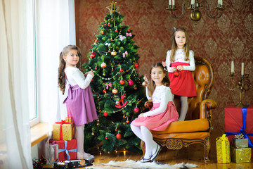 Fototapeta na wymiar Three sisters decorate the Christmas tree with balls.