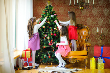 Three sisters decorate the Christmas tree with balls.