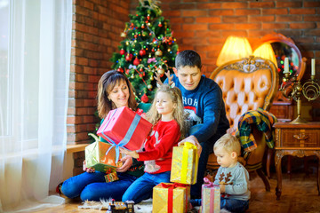 Christmas morning, a big happy family gives each other presents, sitting near the Christmas tree.