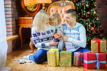Fototapeta na wymiar happy family sitting on the floor near the Christmas tree, giving each other presents and having fun.