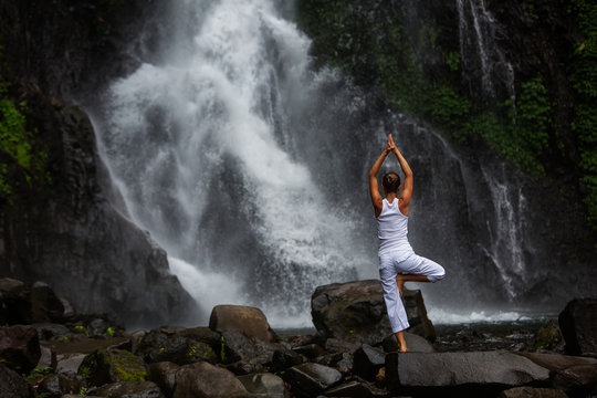 Woman practices yoga at Gitgit waterfall on Bali in indonesia